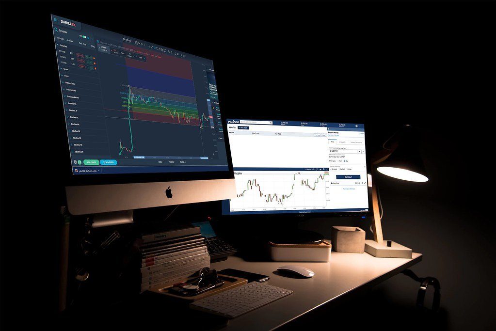 A home trading setup with two monitors showing charts at night