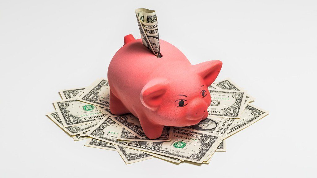 A red piggy bank sitting on a pile of dollar bills