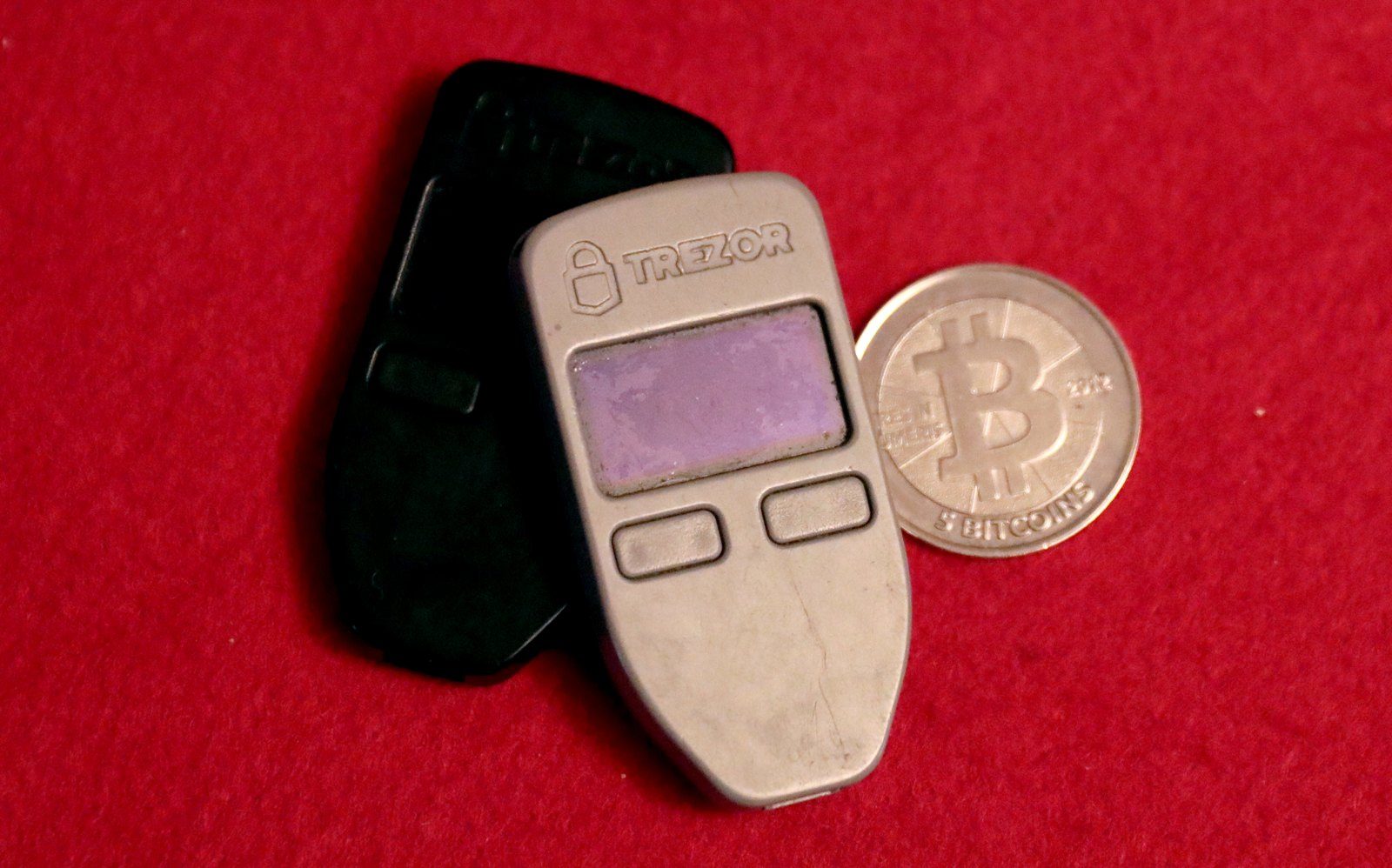 A hardware wallet next to a Bitcoin-style coin on a red background