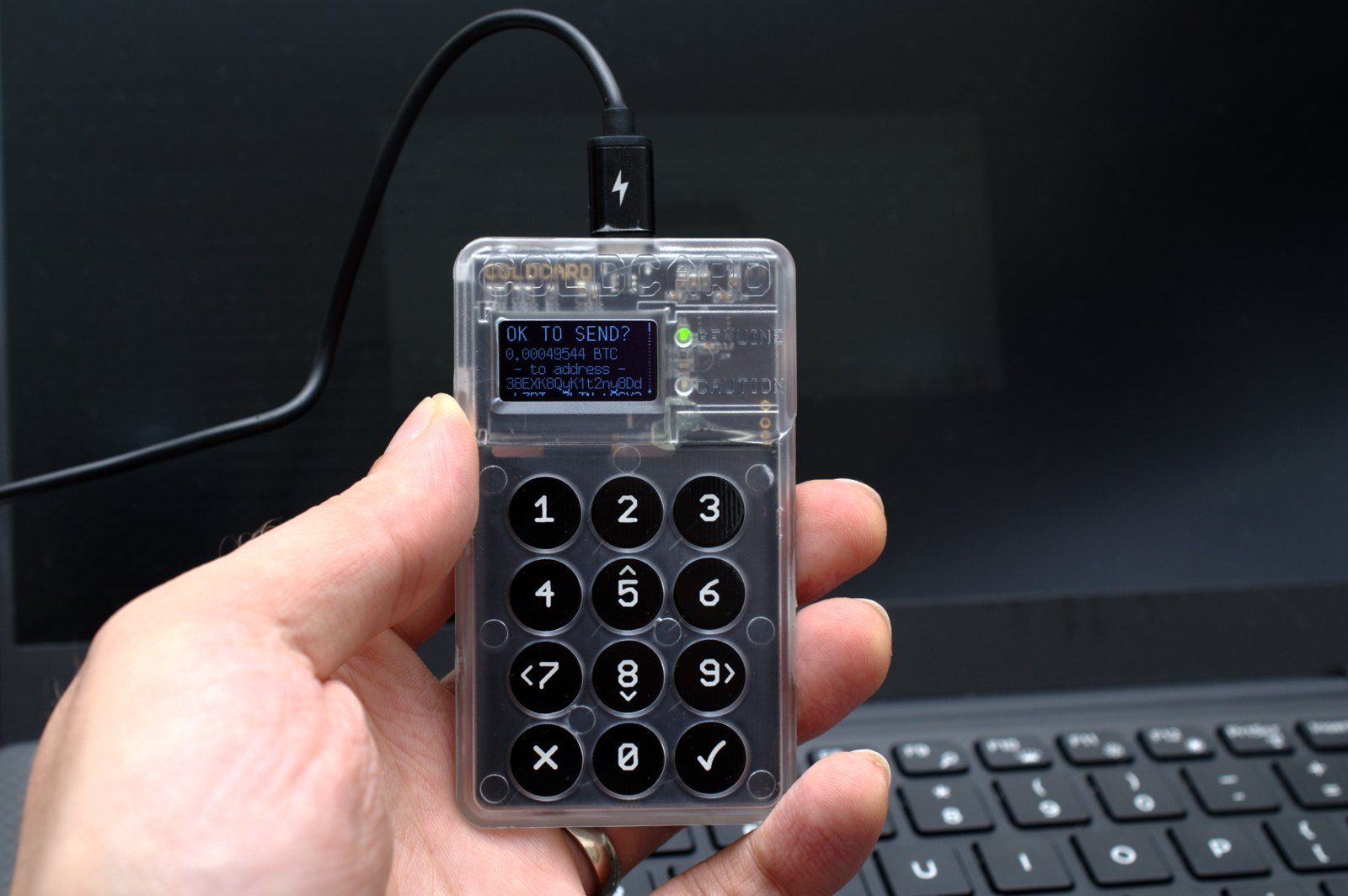 A hand holding a transparent hardware wallet with a keypad